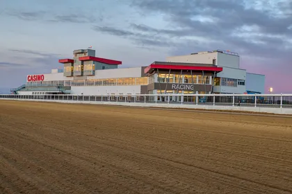 The Century Mile grandstand and casino building seen across the dirt racetrack at dusk, April 2019